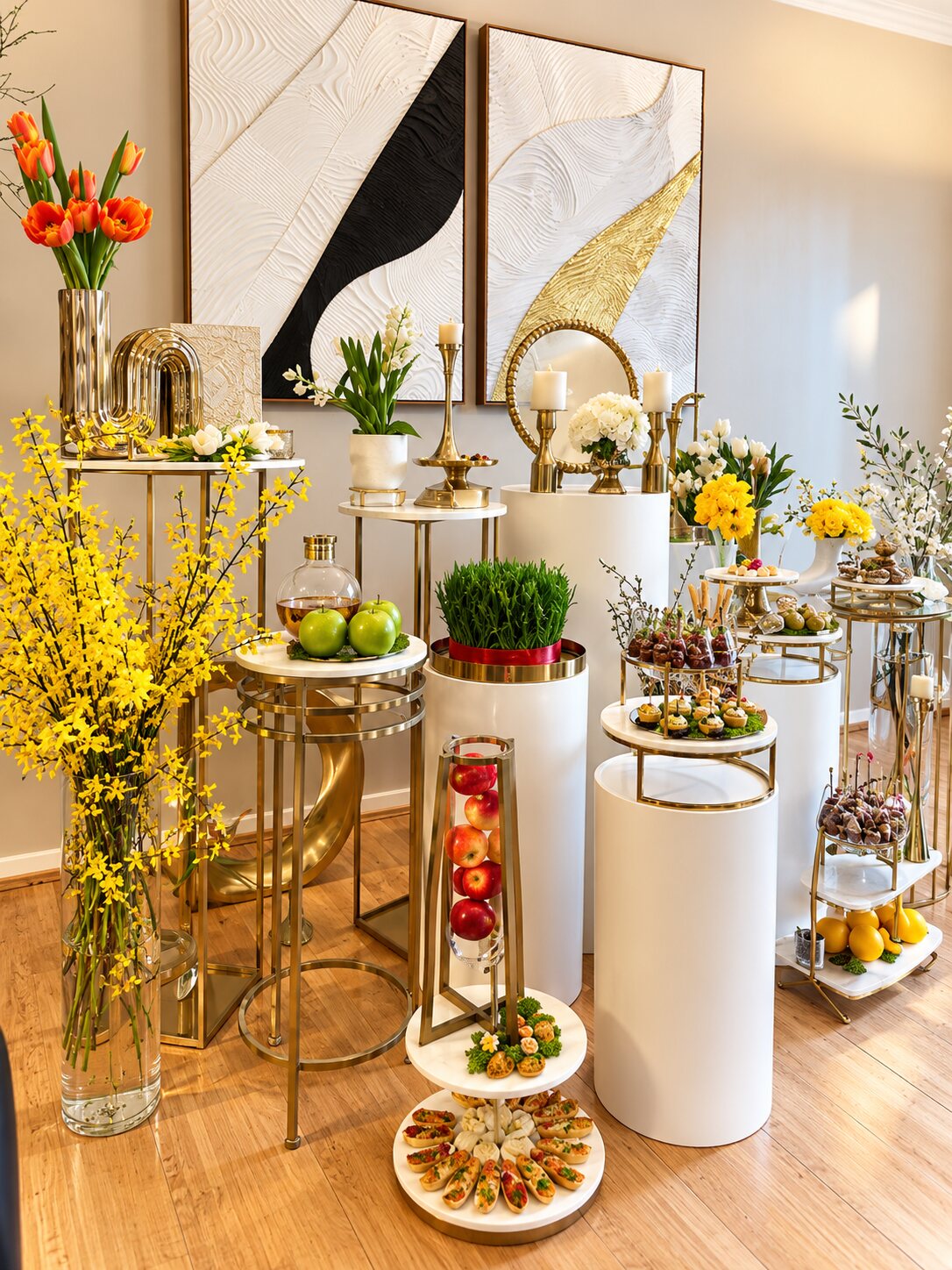 Haft Sin sofreh of white plinths and gold stands with sprouted wheatgrass, apples on a gold tripod, forsythia, tulips, candles and tiered appetizers